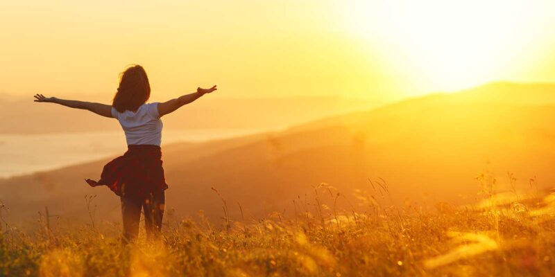 Woman standing confidently in a field on a hill, symbolizing freedom and recovery, as part of an article on using Emotional Freedom Techniques (EFT) for addiction recovery.