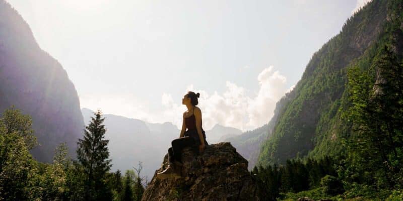 Woman practicing mindfulness and self-compassion while sitting on a rock in the mountains