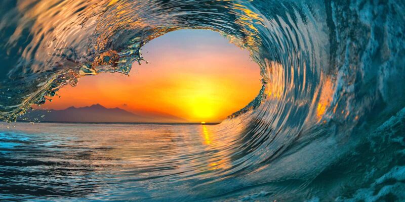 A curling wave at sunset, symbolizing the mindfulness technique of urge surfing where one rides out their urges rather than giving into them.